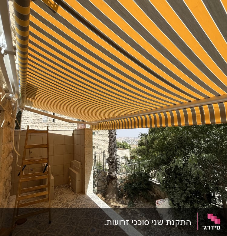 סוכך פסים צהוב ואפור מותקן בחצר